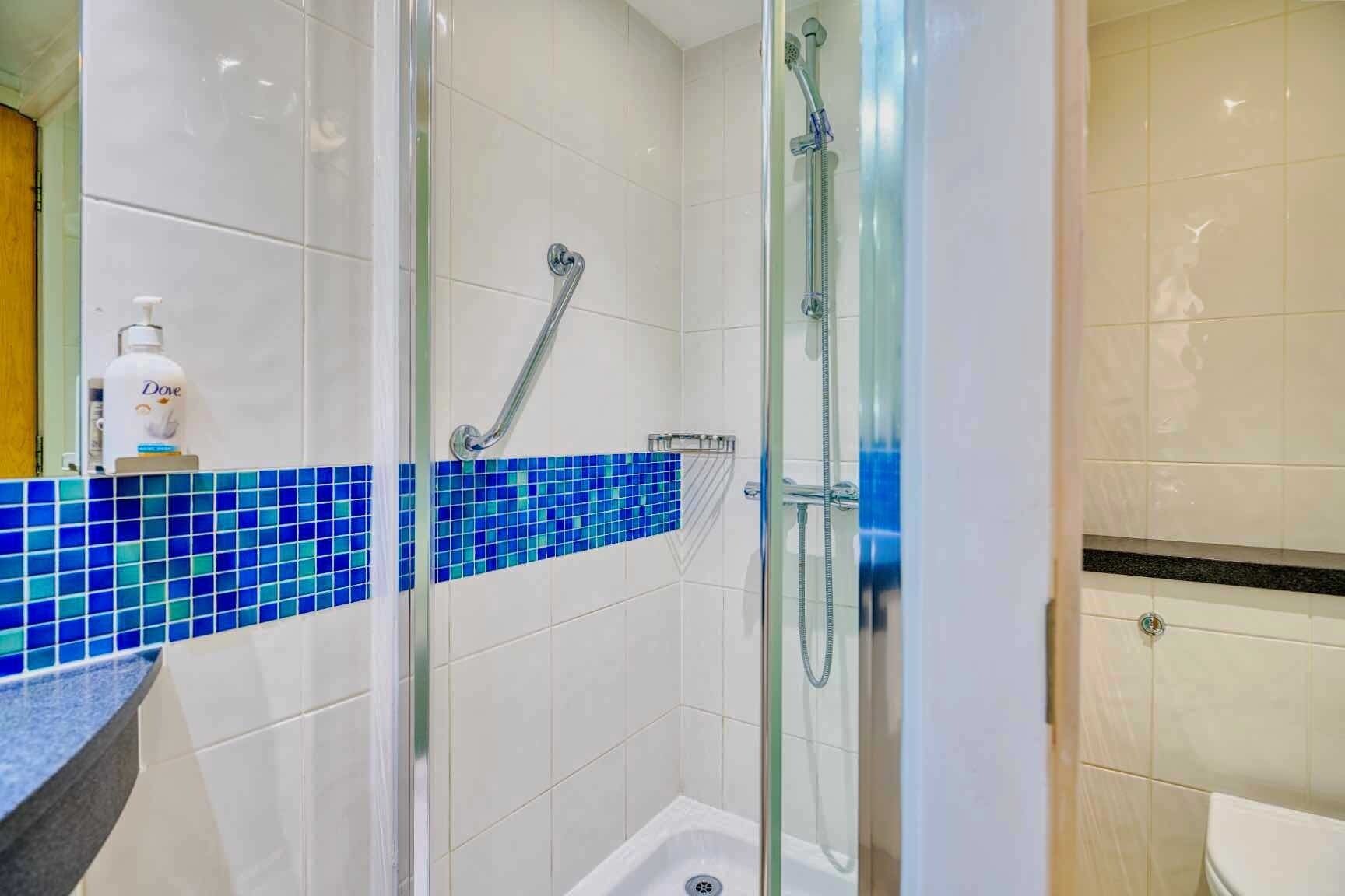 Um banheiro com box de vidro, piso em azulejo e parede decorada com azulejos azuis.