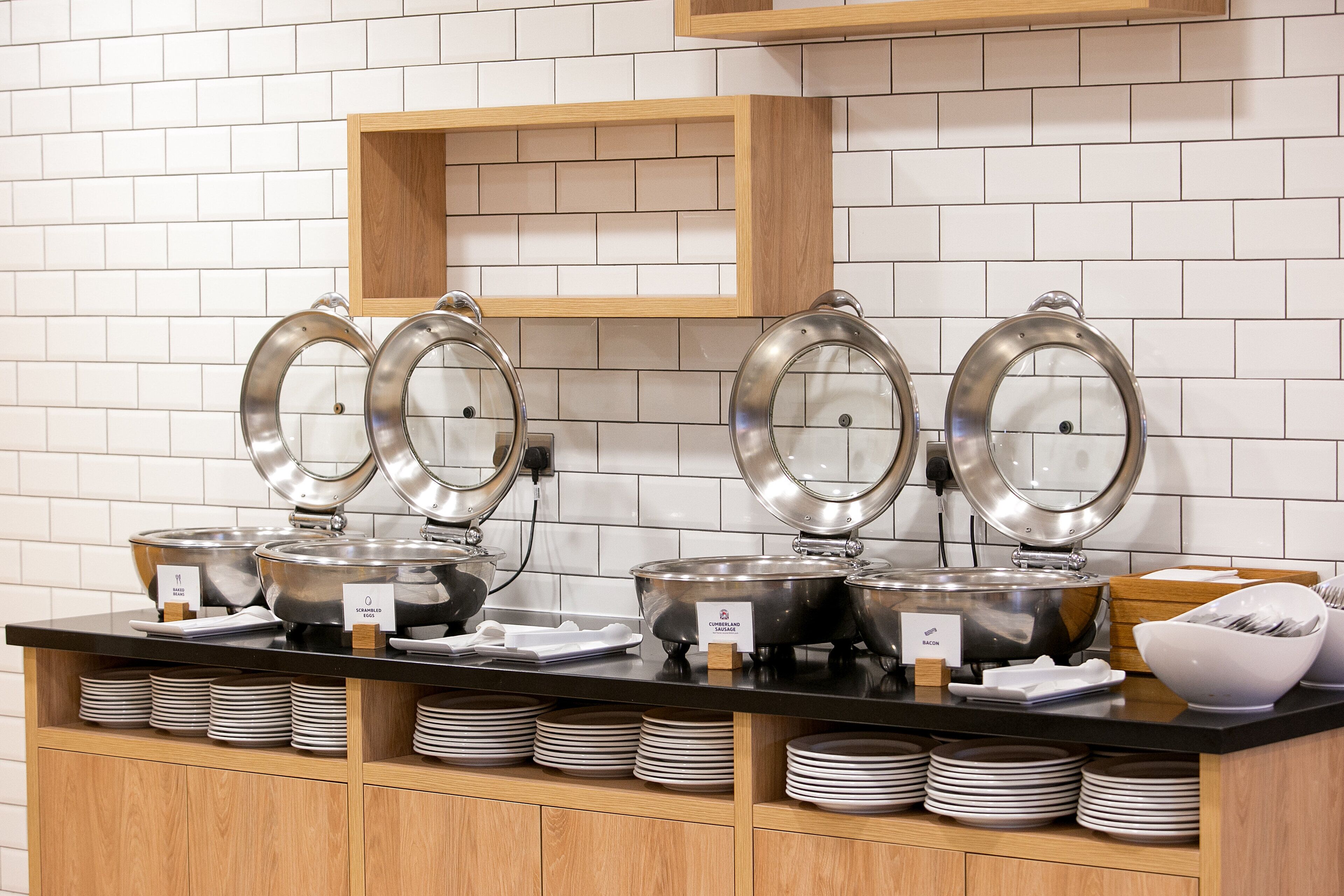 A buffet setup with multiple food stations, including labeled bowls for different dishes, and a counter with stacked plates.