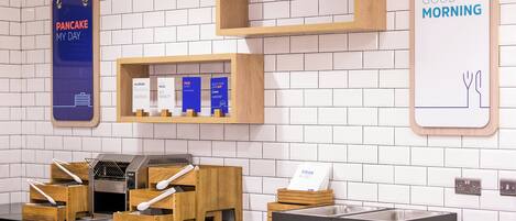 Un área de desayuno con mostrador, una máquina para hacer gofres y un cartel que dice 'BUENOS DÍAS'.