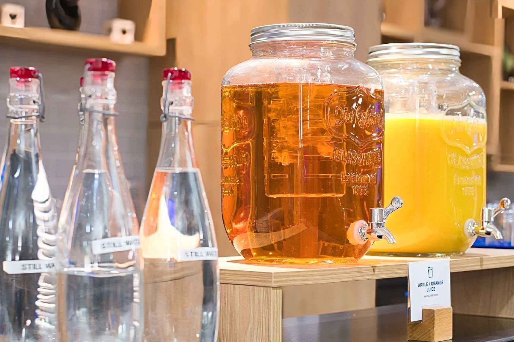 Ett urval av glasvaror med etiketter, en stor behållare med en bärnstensfärgad vätska och en skylt som anger att det är äpple- eller apelsinjuice.