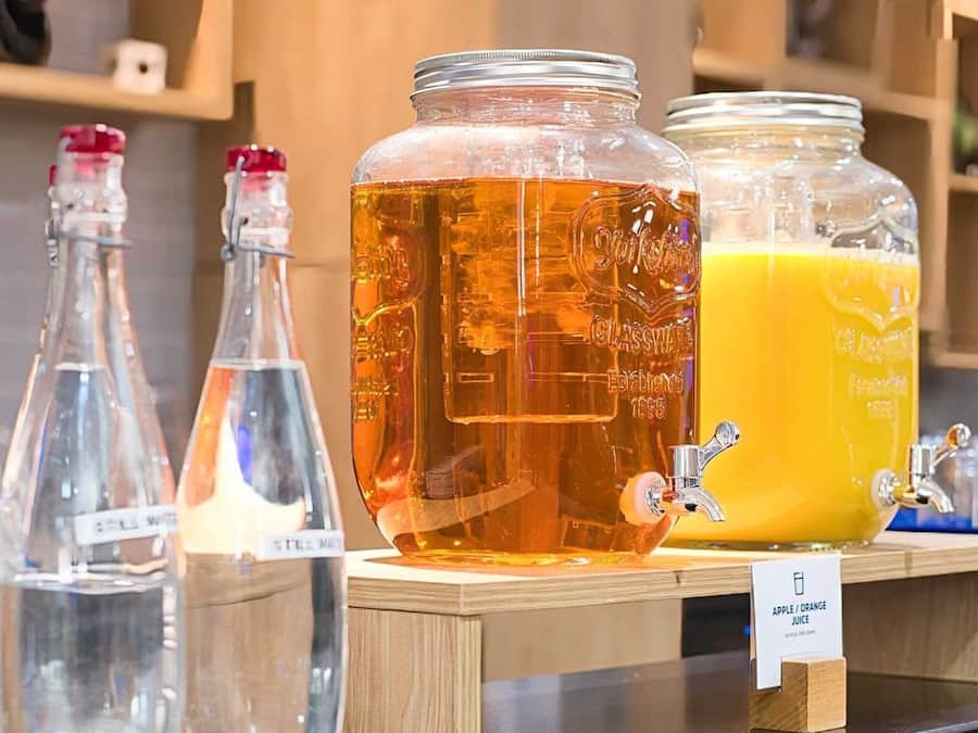 A selection of glassware with labels, a large amber-colored liquid container, and a sign indicating apple/orange juice.