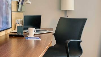 Habitación de hotel con escritorio de madera, una laptop, un control remoto, una taza blanca y una silla negra.