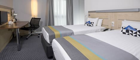 A hotel room with two beds, a desk, a chair, a television, and a window with curtains.