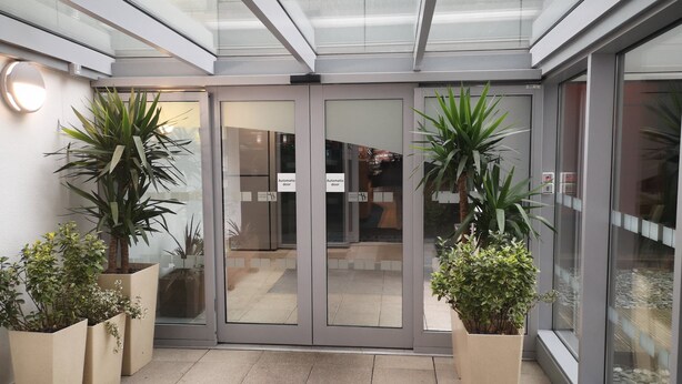 A modern hotel entrance with automatic doors, potted plants, and a glass ceiling.