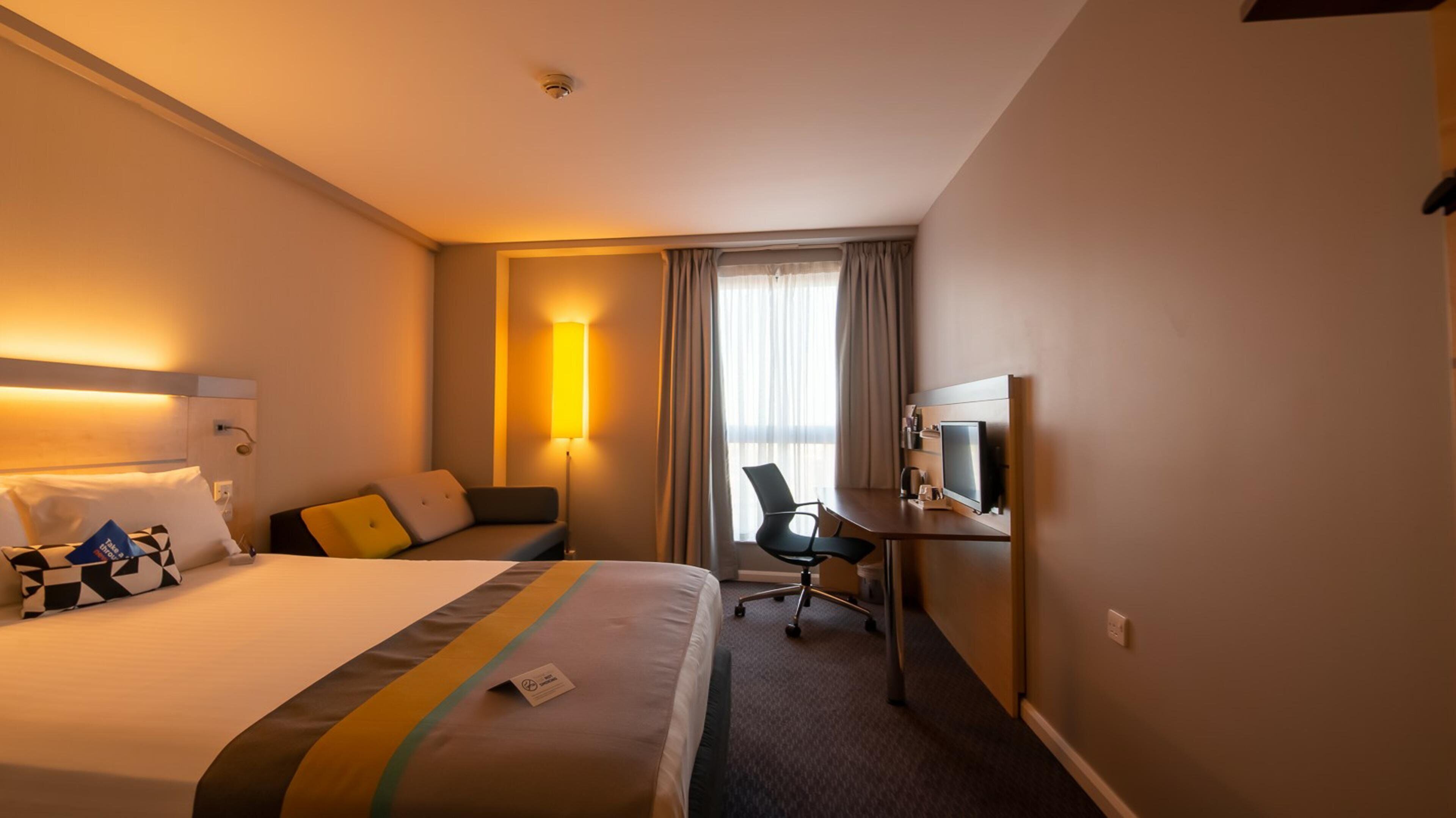 Una habitación de hotel con una cama, un escritorio con una computadora, una silla y un televisor.