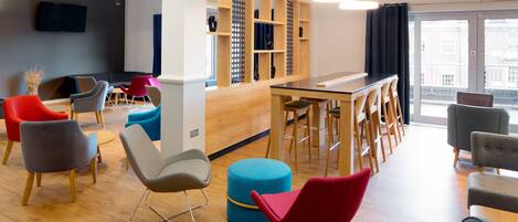 A modern lounge area with a variety of seating options, a bar, and a large window offering a view of the city.
