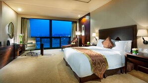 A hotel room with a large bed, a desk, a chair, and a view of the city at dusk. - Jin Jiang International Hotel Xi'an (Xi'an)