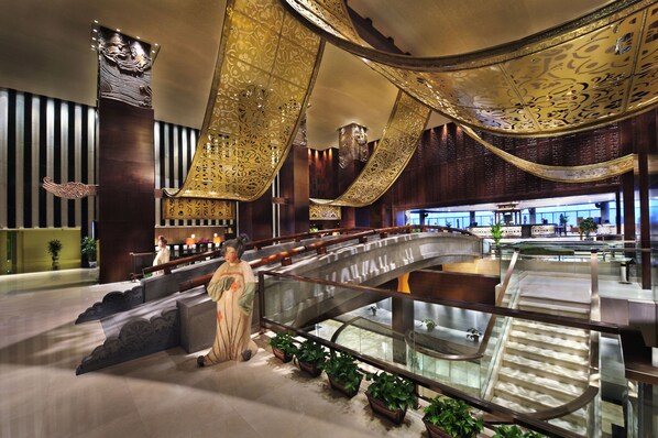 Eine moderne Hotellobby mit einer zentralen Treppe, dekorativen Deckenverzierungen und einer Statue.