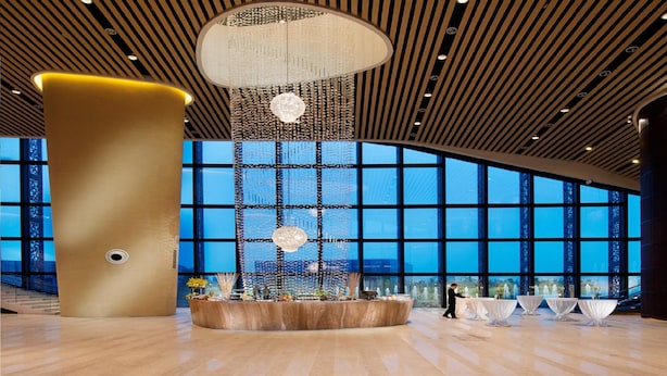 A spacious lobby with a large wooden pillar, a decorative hanging light fixture, and a view of the city through large windows. - Jin Jiang International Hotel Xi'an (Xi'an)