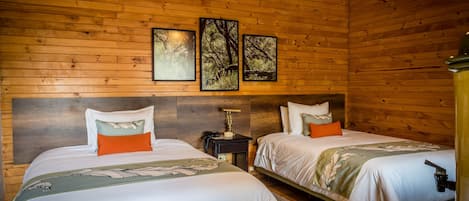 Una habitación de cabaña de madera con dos camas, una mesita de noche, una lámpara y cuadros en la pared.