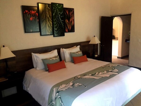 Una habitación de hotel con una cama grande, dos lámparas de noche, un cabecero y tres cuadros en la pared.