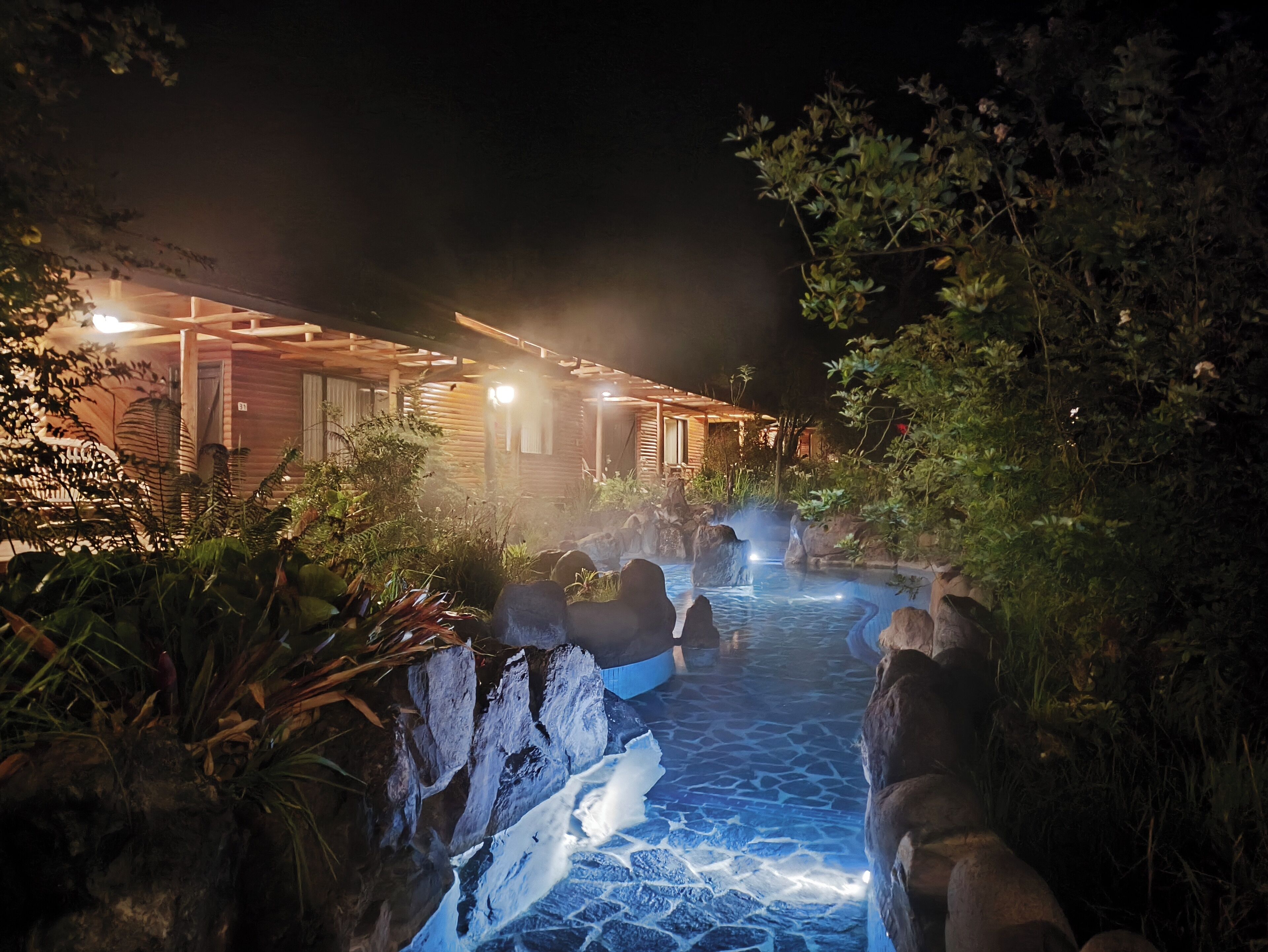 Une vue nocturne d’un chalet rustique en bois avec une source d’eau chaude.