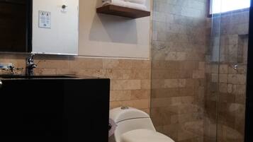 A modern bathroom with a toilet, sink, and shower. There are towels on a shelf and a glass shower enclosure.