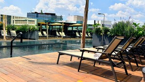 A rooftop pool area with lounge chairs and umbrellas, surrounded by potted plants and modern buildings. - Hive Nápoles By G Hotels (Mexico City)