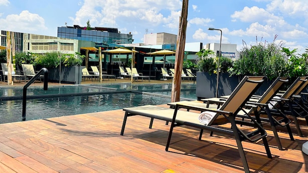 A rooftop pool area with lounge chairs and umbrellas, surrounded by potted plants and modern buildings. - Hive Nápoles By G Hotels (Mexico City)