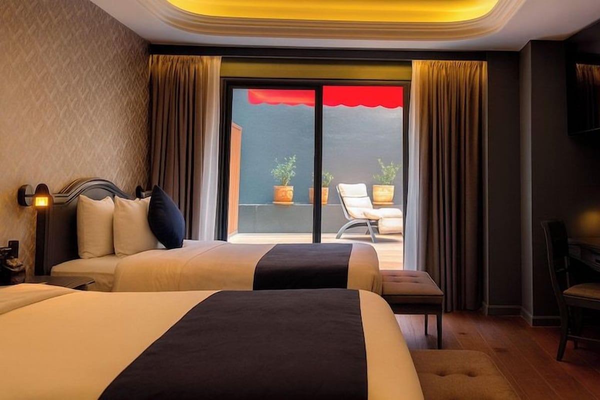 Habitación de hotel con dos camas, un escritorio, una silla y un balcón con vistas.