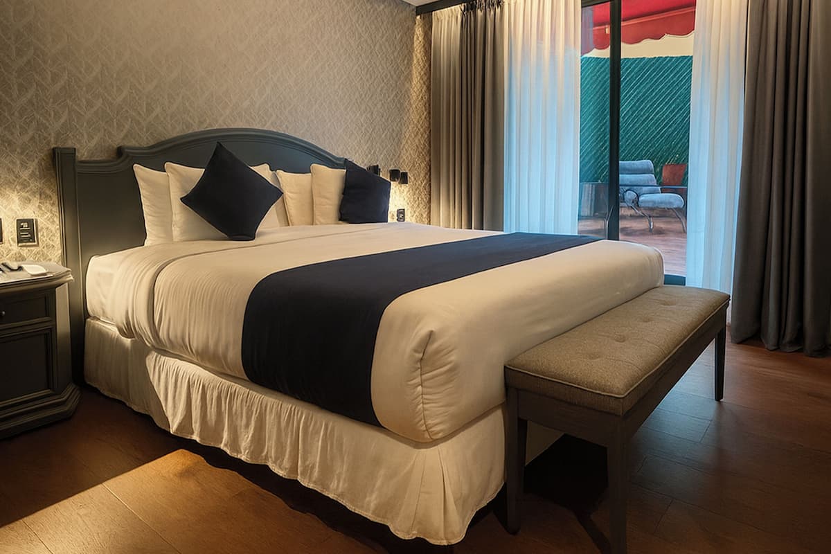 A large bed with a bench, a nightstand, and a view of the outdoors through a window.