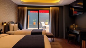 A hotel room with two beds, a desk, a chair, a TV, and a balcony with a red awning. - Hive Nápoles By G Hotels (Mexico City)