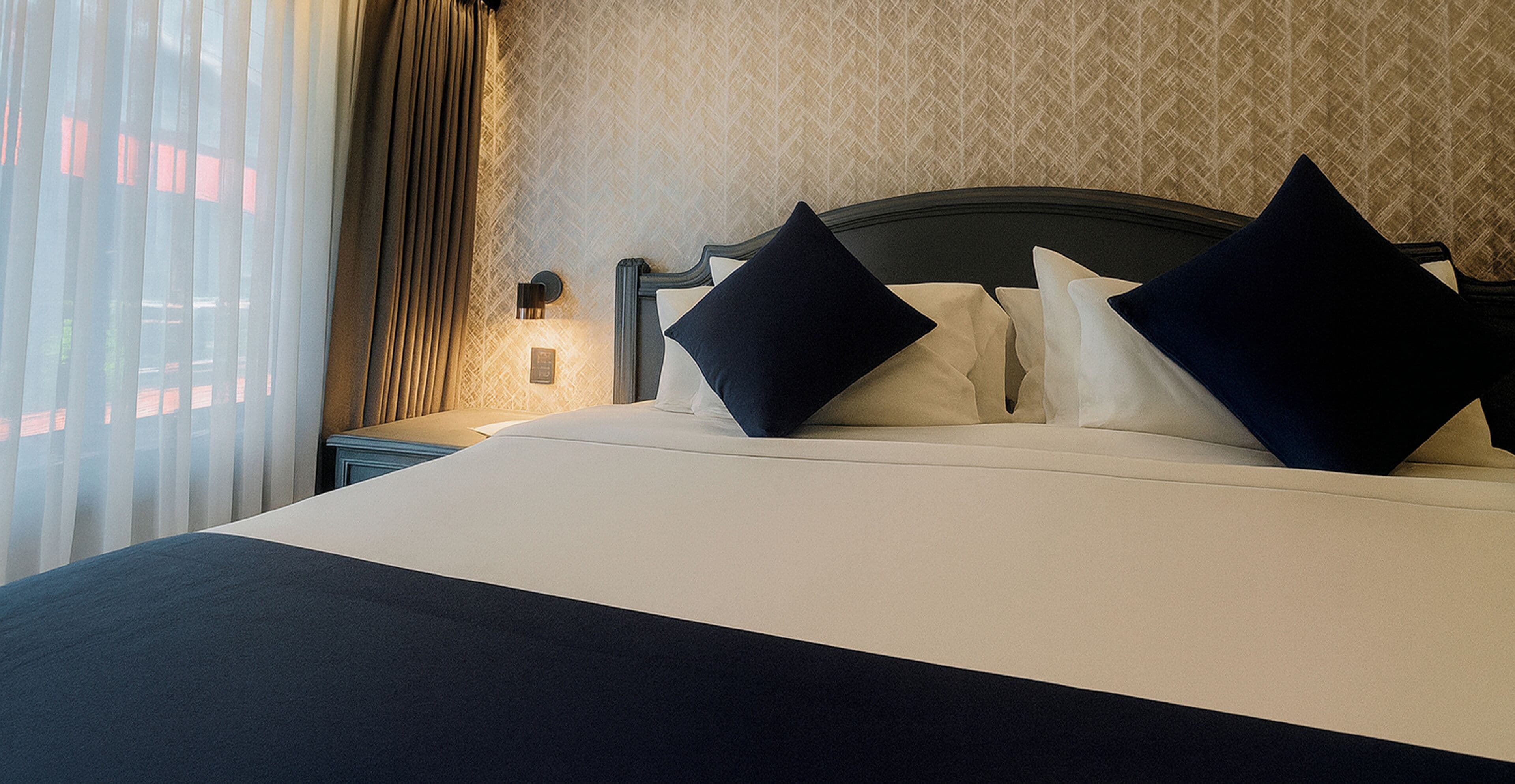 Une chambre d’hôtel avec un lit bien fait, une table de chevet avec une lampe et une fenêtre avec des rideaux.