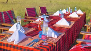 An outdoor dining setup with tables, chairs, and a view of a grassy field. - Muthu Keekorok Lodge, Maasai Mara, Narok (Maasai Mara)