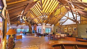 A spacious lobby with a high wooden ceiling and stone walls, featuring a reception desk, seating areas, and artwork on the walls. - Muthu Keekorok Lodge, Maasai Mara, Narok (Maasai Mara)