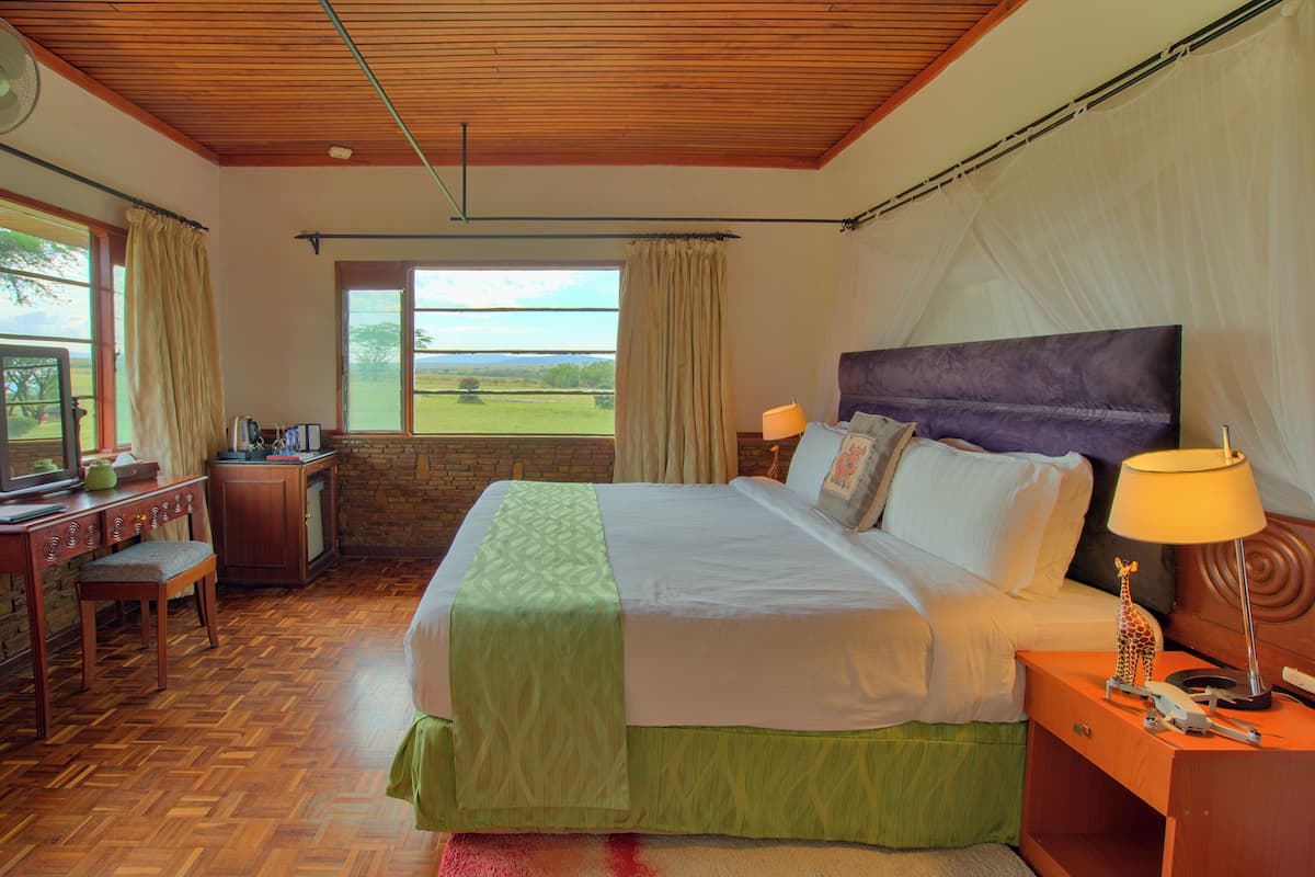 Relax in a spacious room with a large bed, wooden desk, and a window offering a view of the outdoors.