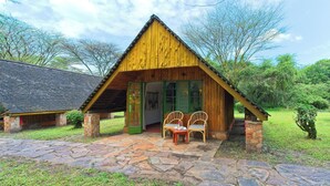 Una cabaña de madera rústica con entrada empedrada de piedra, dos sillas de mimbre y una pequeña mesa.