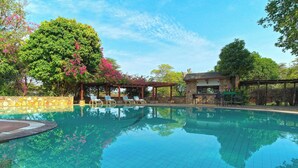 A clear swimming pool with lounge chairs and a pergola, surrounded by trees and a stone wall. - Muthu Keekorok Lodge, Maasai Mara, Narok (Maasai Mara)