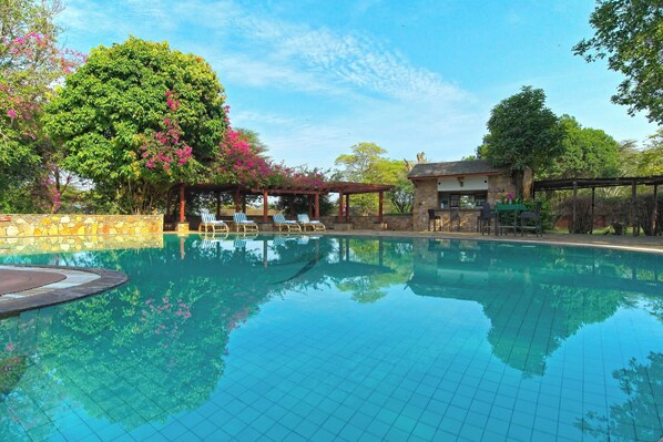 A clear swimming pool with lounge chairs and a pergola, surrounded by trees and a stone wall. - Muthu Keekorok Lodge, Maasai Mara, Narok (Maasai Mara)