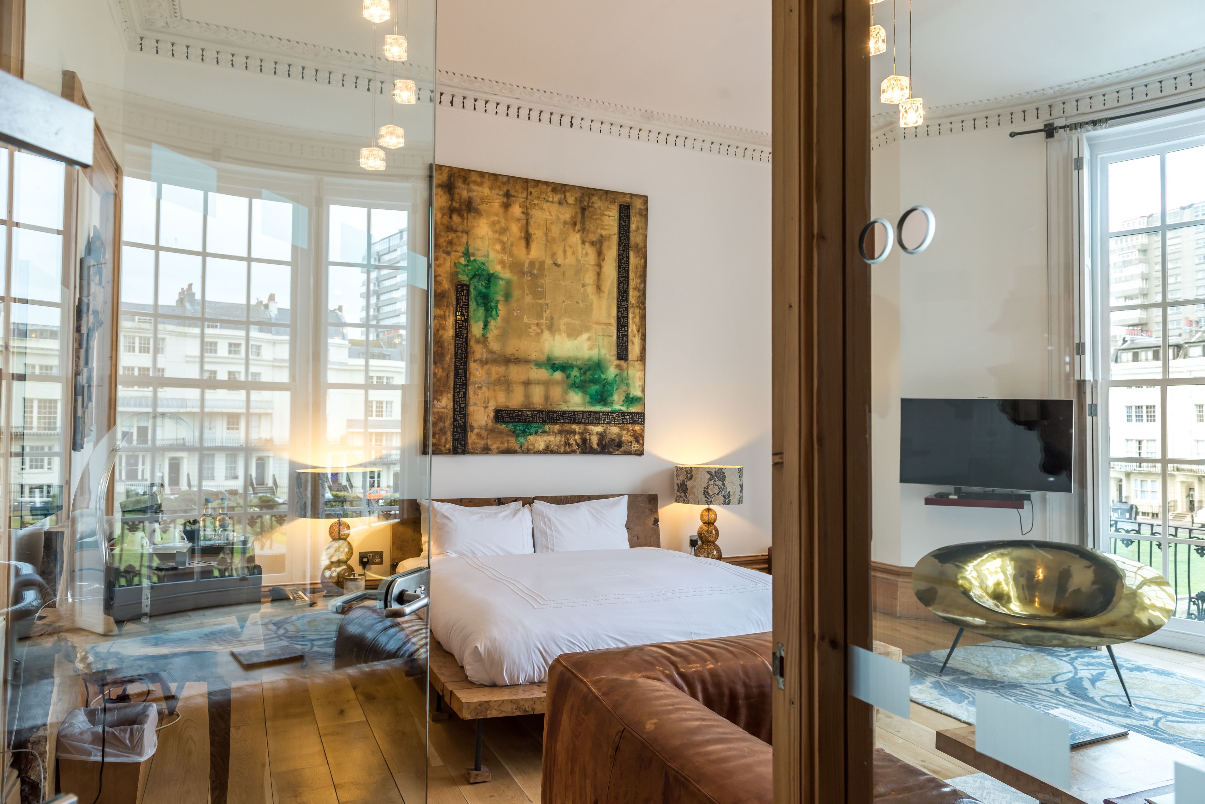A modern hotel room with a large bed, a sofa, a TV, and a view of the city through large windows.