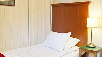 Ein Einzelbett mit Holz-Kopfteil, ein Nachttisch mit Lampe und eine rote Tagesdecke.
