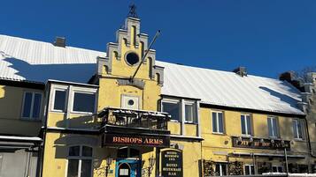 Un bâtiment jaune sur lequel on peut lire l’inscription suivante : « HÔTEL-RESTAURANT-BAR BISHOP’S ARMS ».