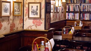 A restaurant with wooden tables, wicker baskets, framed pictures, and a bookshelf in the background. - Hotel Bishops Arms Kristianstad (Kristianstad)