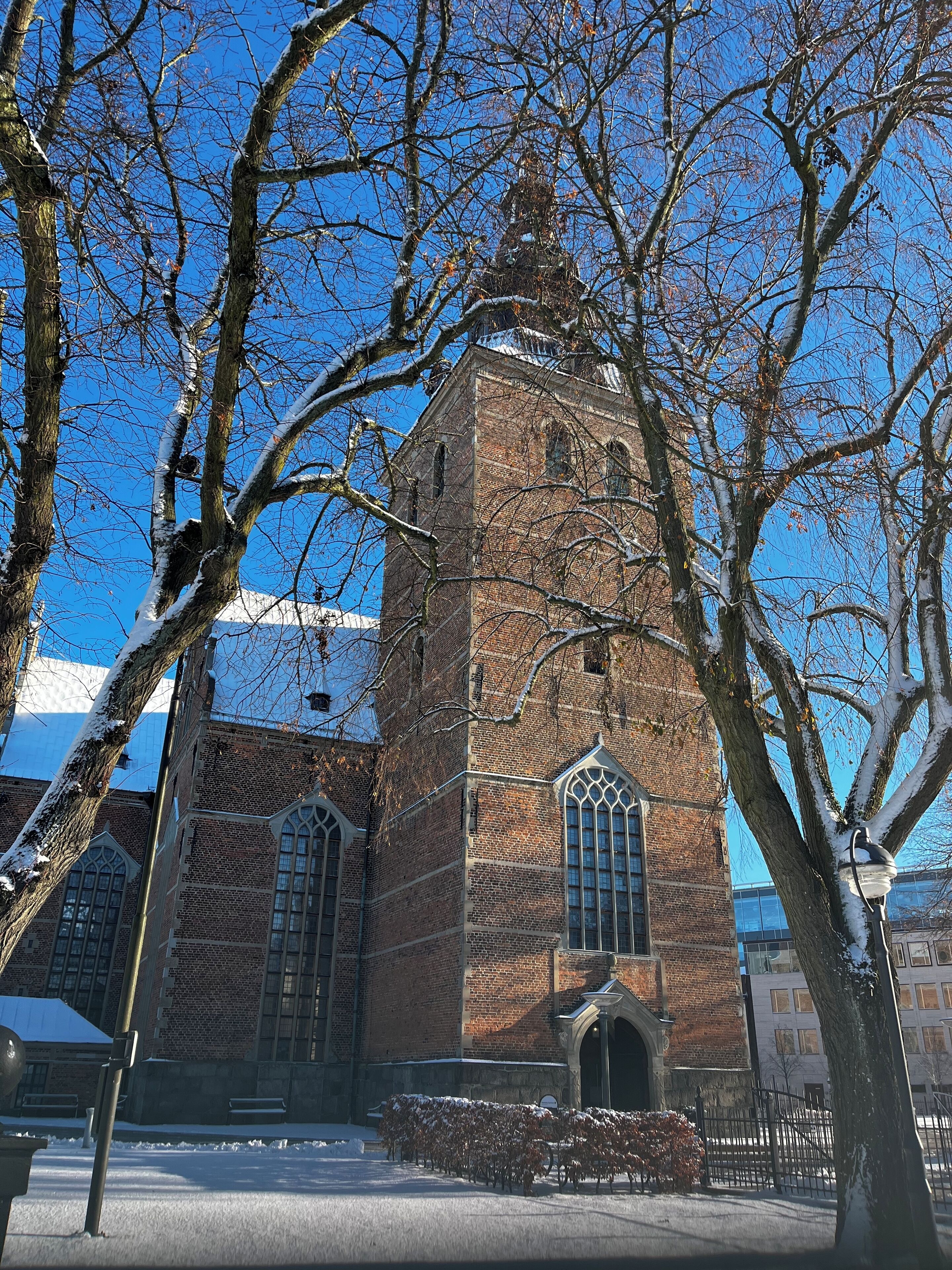 A brick building with arched windows and a tower, surrounded by bare trees and a clear blue sky.