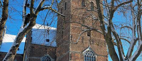 A brick building with arched windows and a tower, surrounded by bare trees and a clear blue sky.