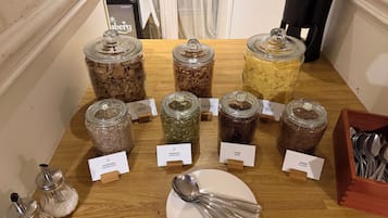 Una mesa de madera con diversos alimentos en frascos de vidrio, cada uno etiquetado con el tipo de comida y su origen.
