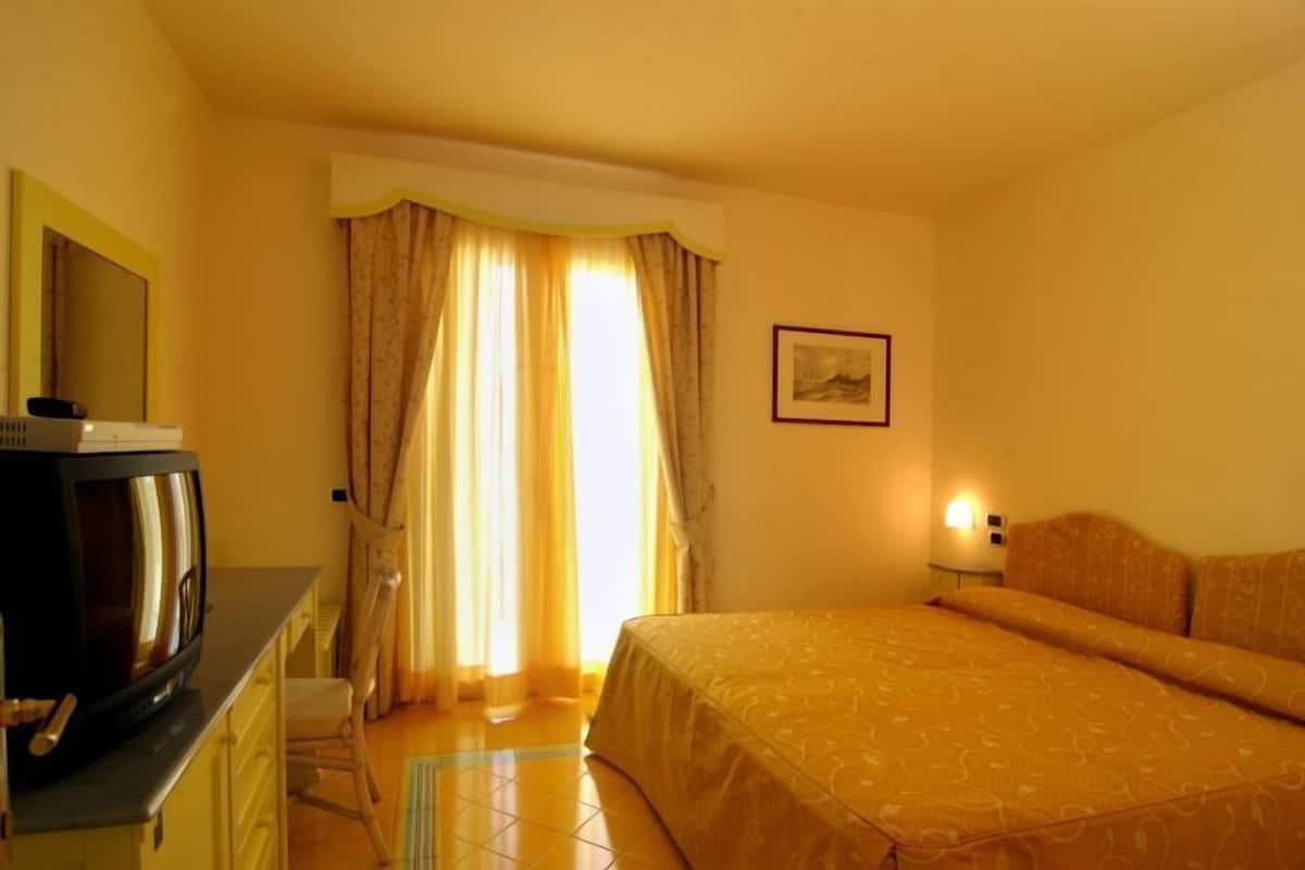 Ein Hotelzimmer mit Bett, Fernseher, Schreibtisch und einem Fenster mit Vorhängen.