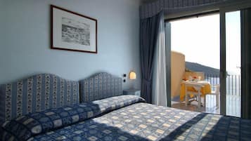 Una habitación de hotel con una cama grande, una mesita con una silla, y un balcón con mesa y sillas.