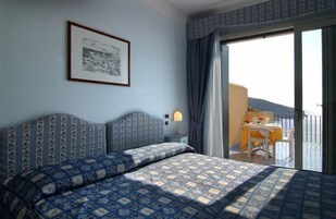 Una habitación de hotel con una cama grande, una mesita con una silla, y un balcón con mesa y sillas.