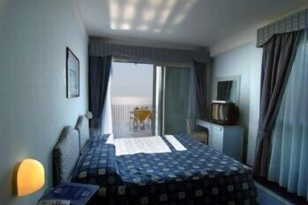 Ein Hotelzimmer mit Bett, Schreibtisch, Stuhl, Fernseher und Blick auf den Außenbalkon.