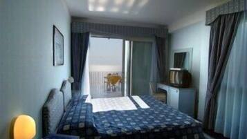 A hotel room with a bed, a desk, a chair, a television, and a view of the outside balcony.