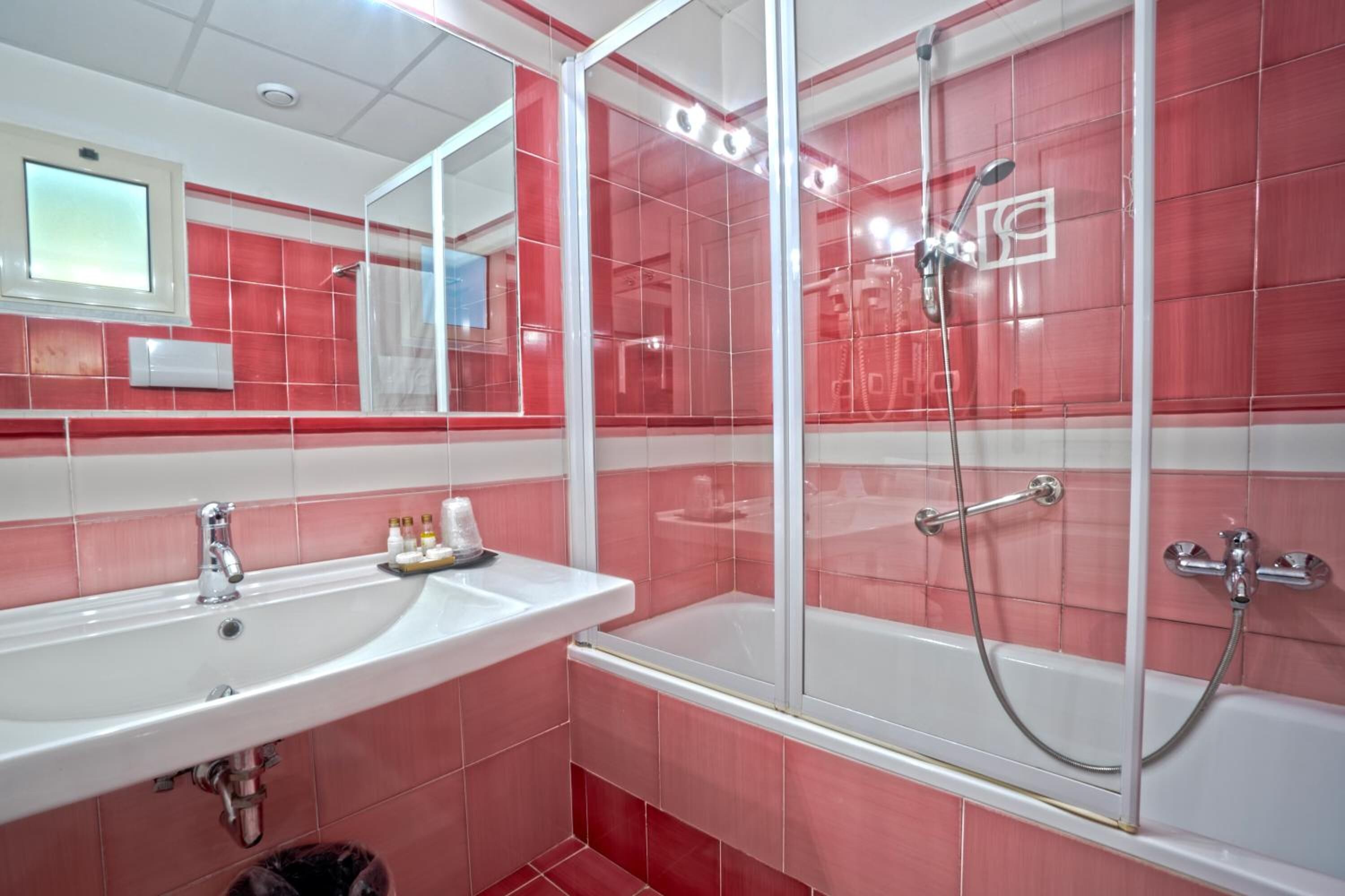 A bathroom with a white sink, a glass-enclosed shower, and red-tiled walls.