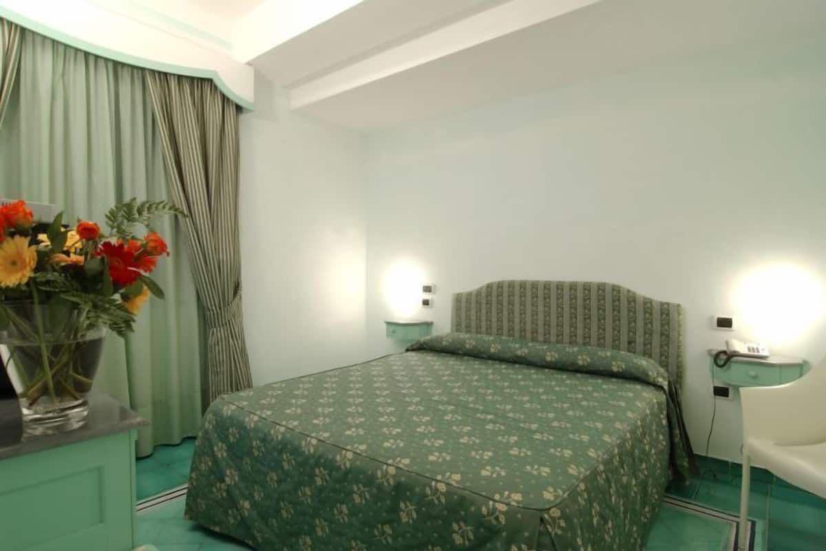 Ein Zimmer mit einem Bett, einem Nachttisch, einem Stuhl und einem Blumenstrauß.