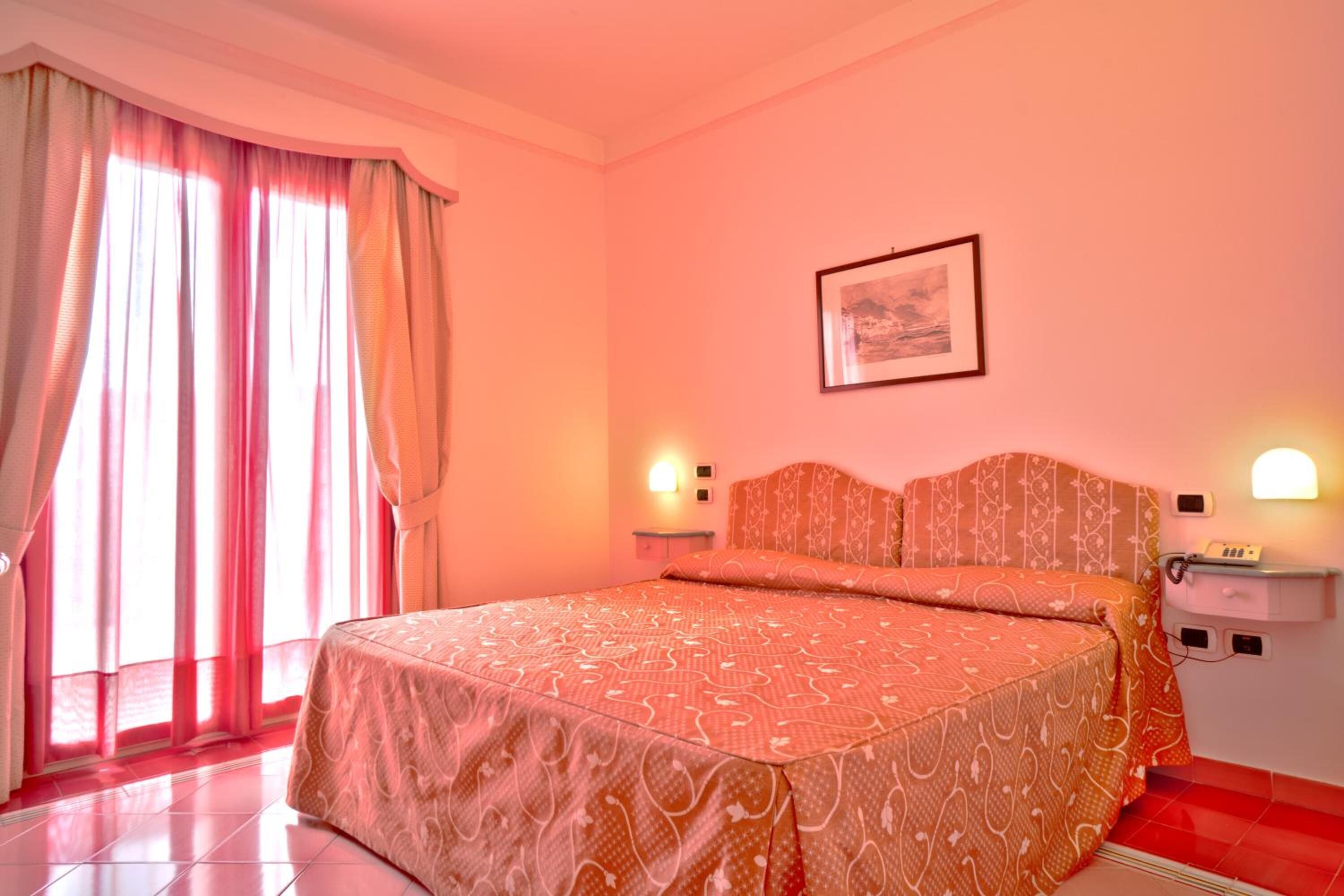A bedroom with a large bed, two bedside lamps, a nightstand, and a framed picture on the wall.