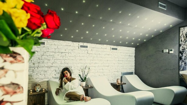 Un cuarto de spa con pared de ladrillo blanco, dos sillones blancos acolchados, una mesita con un florero y un techo con iluminación empotrada.