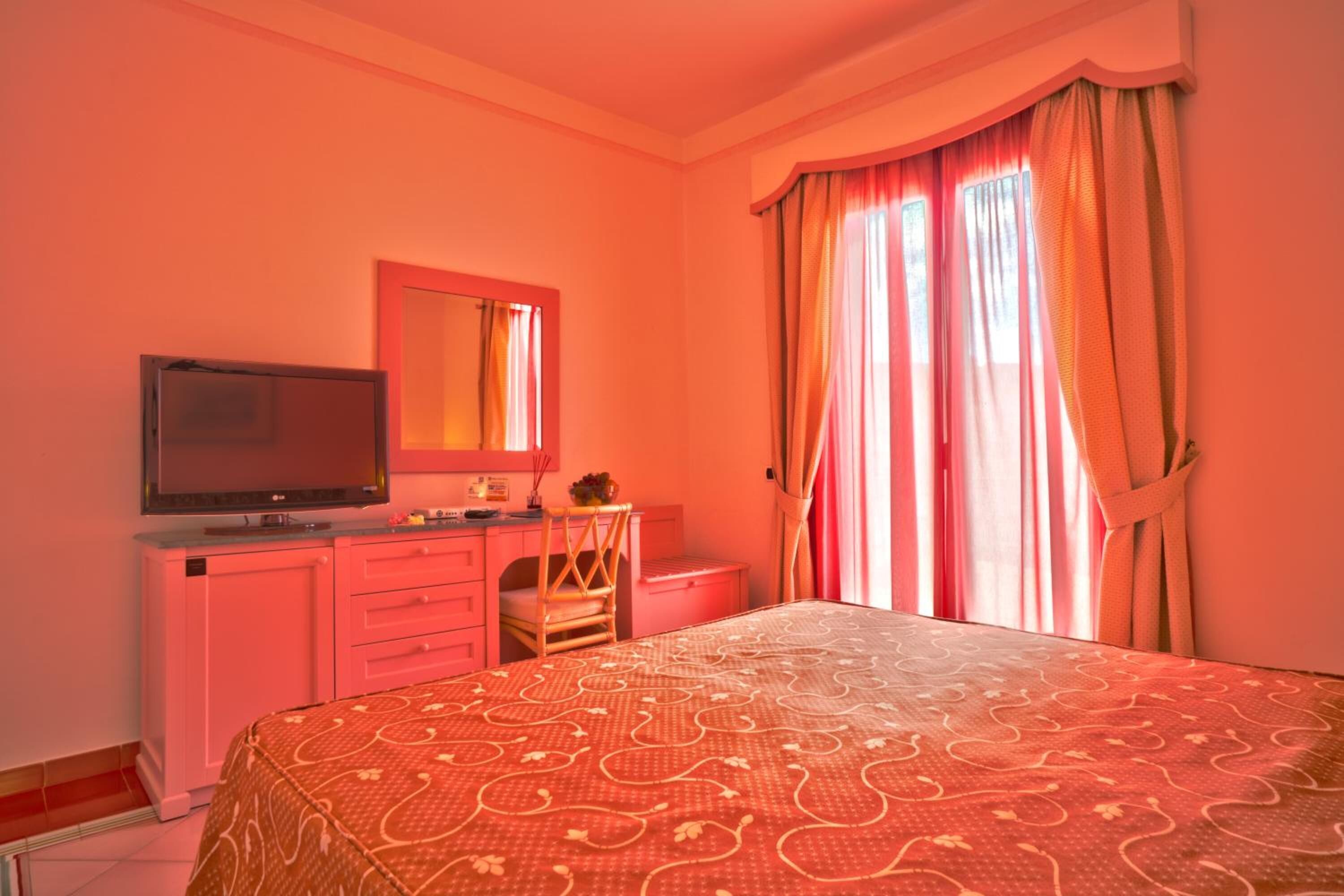 Une chambre à coucher avec un lit, une télévision, une commode et une fenêtre avec des rideaux.