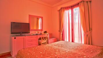 A bedroom with a bed, a television, a dresser, and a window with curtains.