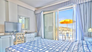 Habitación de hotel con una cama grande, televisión, escritorio y vistas a la playa a través de una puerta corrediza de vidrio.