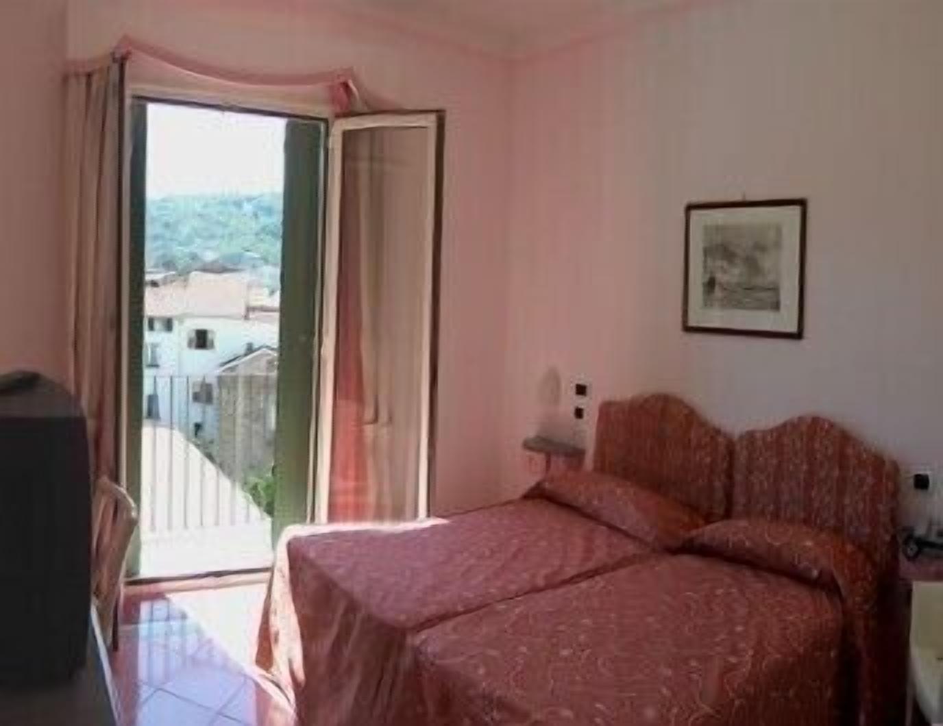 A bedroom with a bed, a chair, a desk, and a window with curtains.