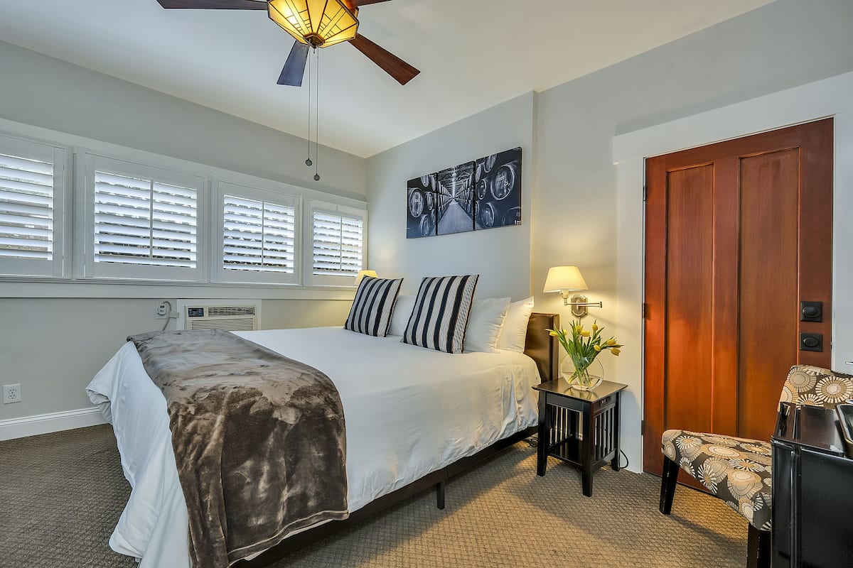 A bedroom with a bed, a chair, a desk, a ceiling fan, and a door.